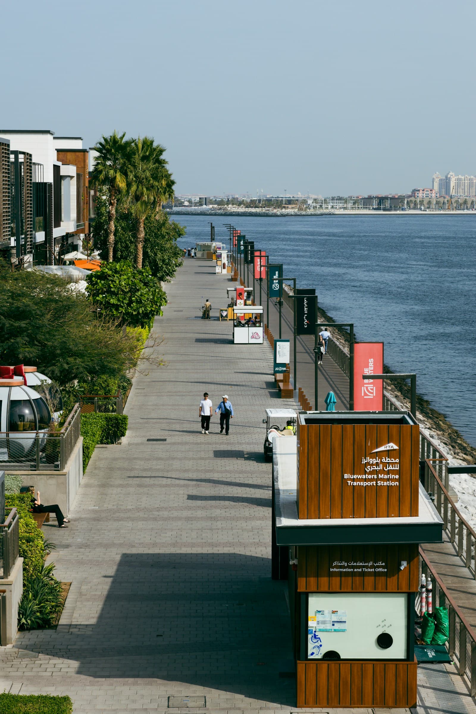 Pedestrians walking along a Dubai waterfront promenade lined with modern buildings β characteristic of The Walk at JBR