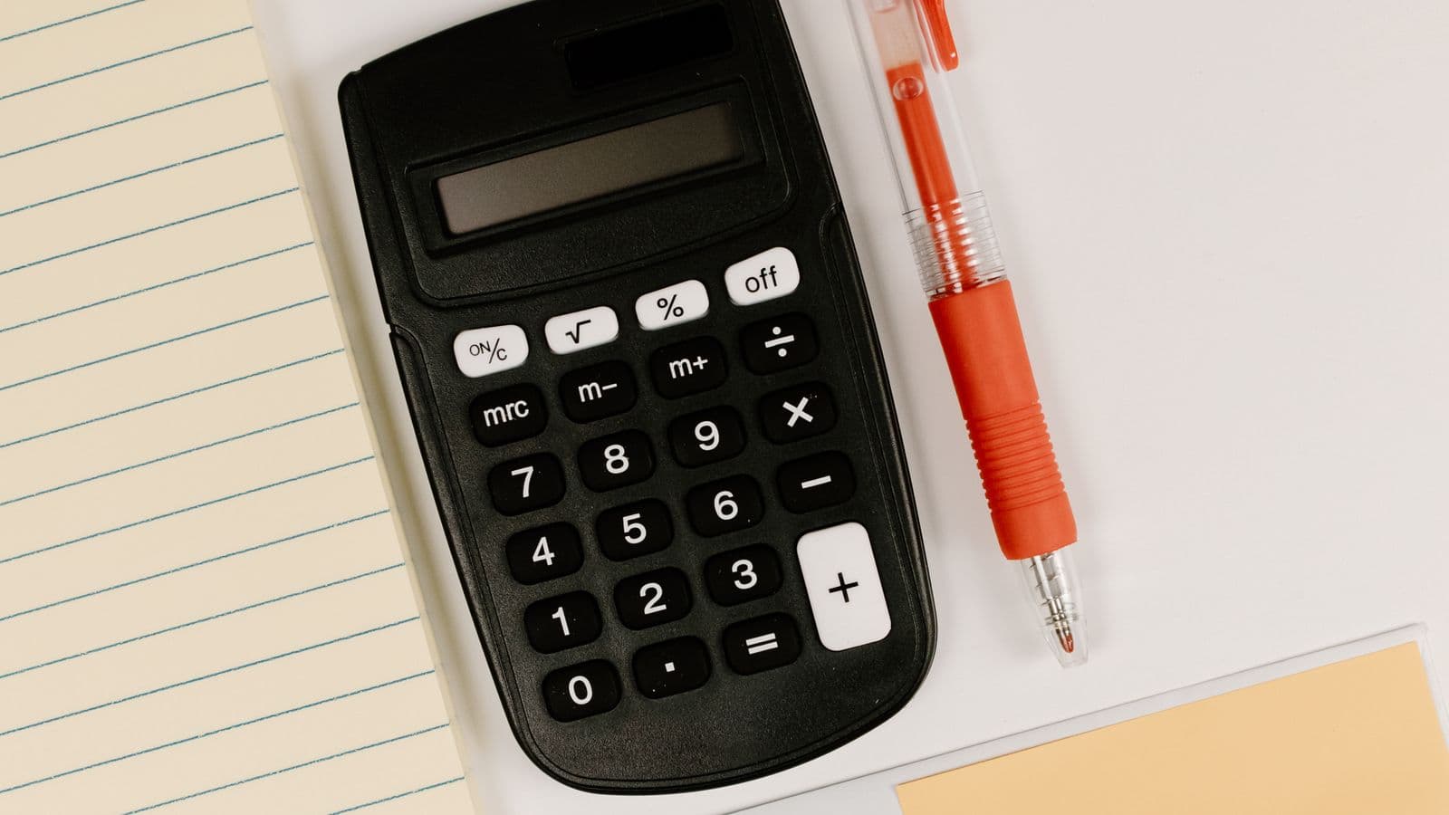 Black calculator with a blank display beside a red pen and a blank lined notepad